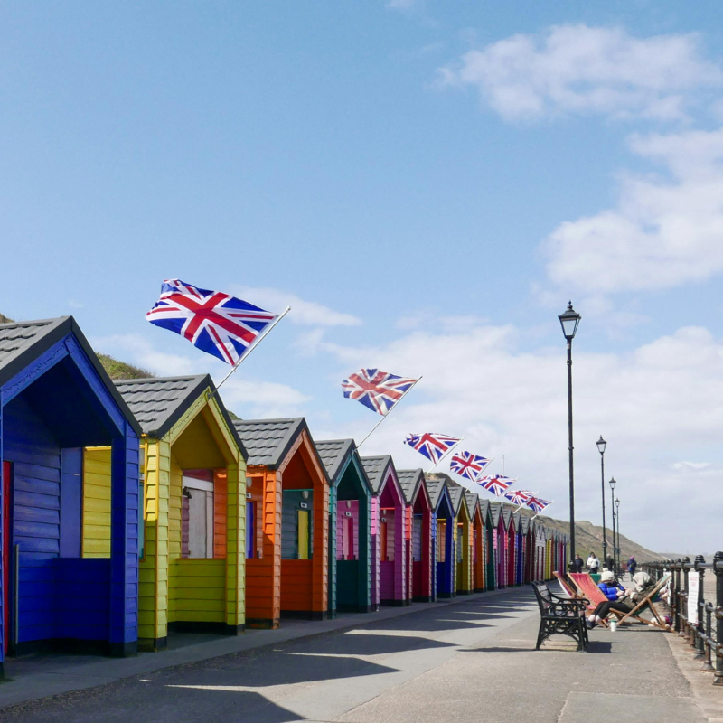 Stock image of a Pier in the United Kingdom, with National Flags above all cabins in the image. Multiple colourful cabins on the left, walkway on the right.